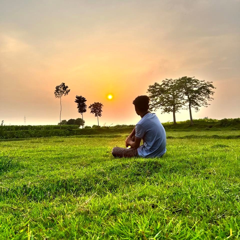 Zihadul Islam sitting alone in a field at sunset